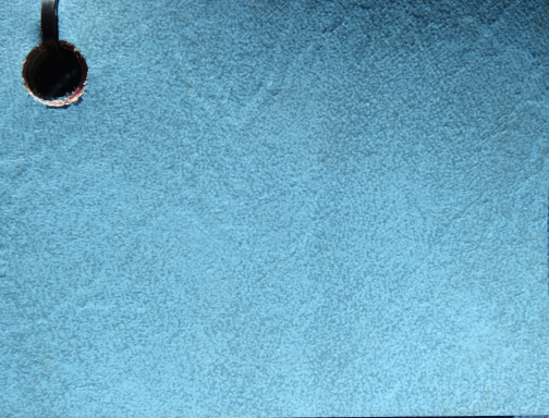 Blue textured surface with a black circular object in the top left corner.